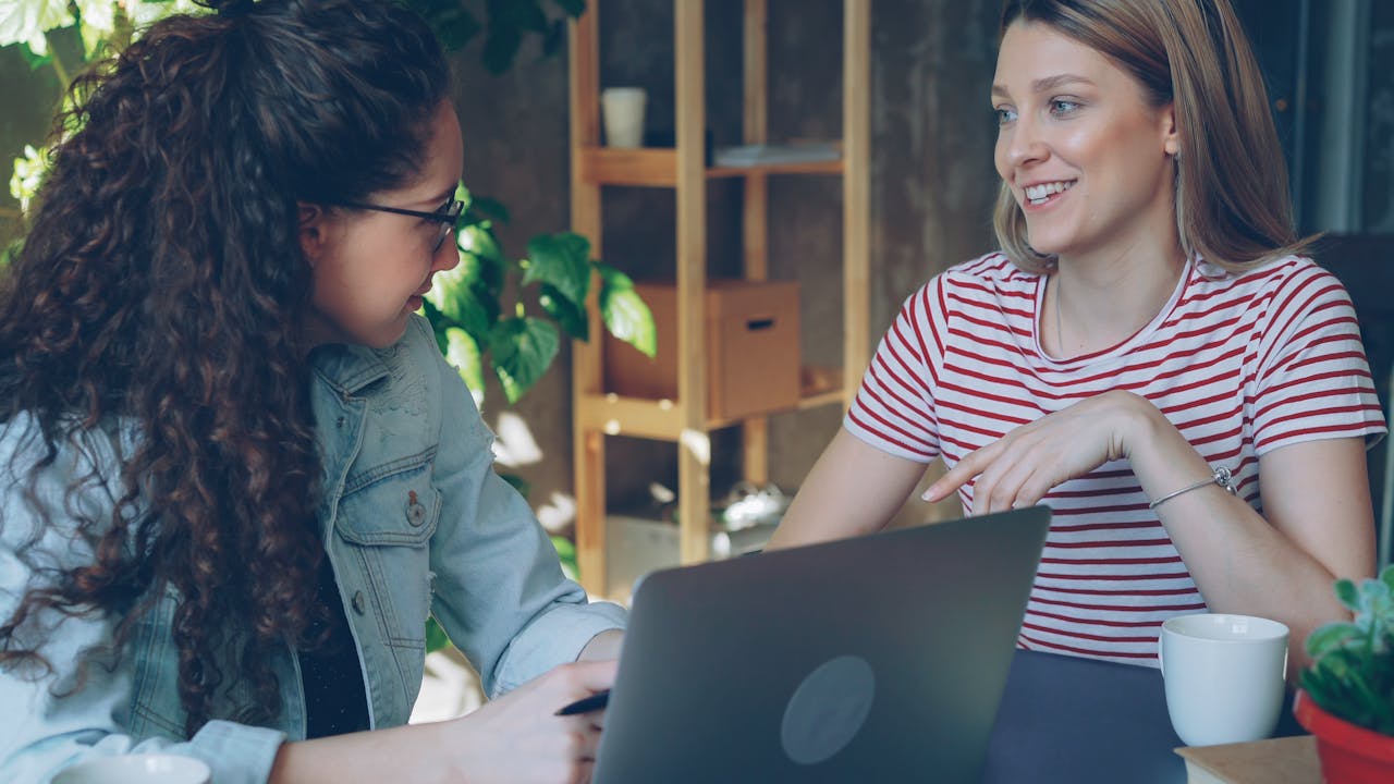 The Art of Drawing Readers In: Your attractive post title goes here Two women engaged in a friendly business meeting indoors with a laptop.